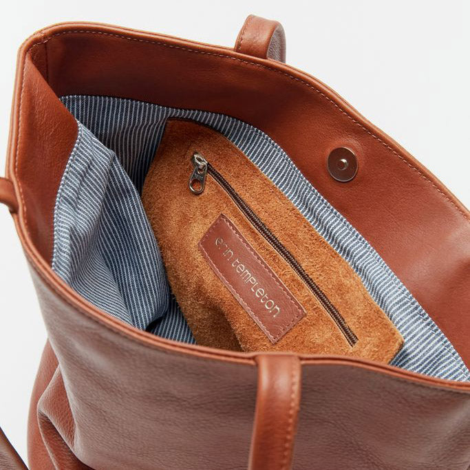 an interior shot of the erin templeton bucket bag, showing a hickory stripe cotton lining, inner leather zip pocket, the erin templeton logo and a magnetic snap closure