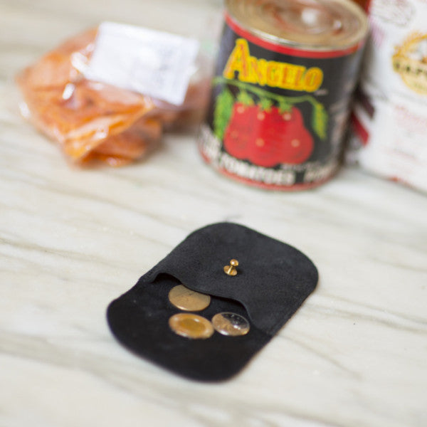 a small leather coin pouch in black leather with a brass stud closure laying open with a few Canadian coins scattered inside, handmade by erin templeton in vancouver, canada
