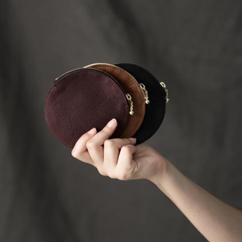 a hand holding three small leather coin purses in chocolate, caramel and black leathers, each with a zip closure in front of a grey backdrop, handmade by erin templeton in vancouver, canada