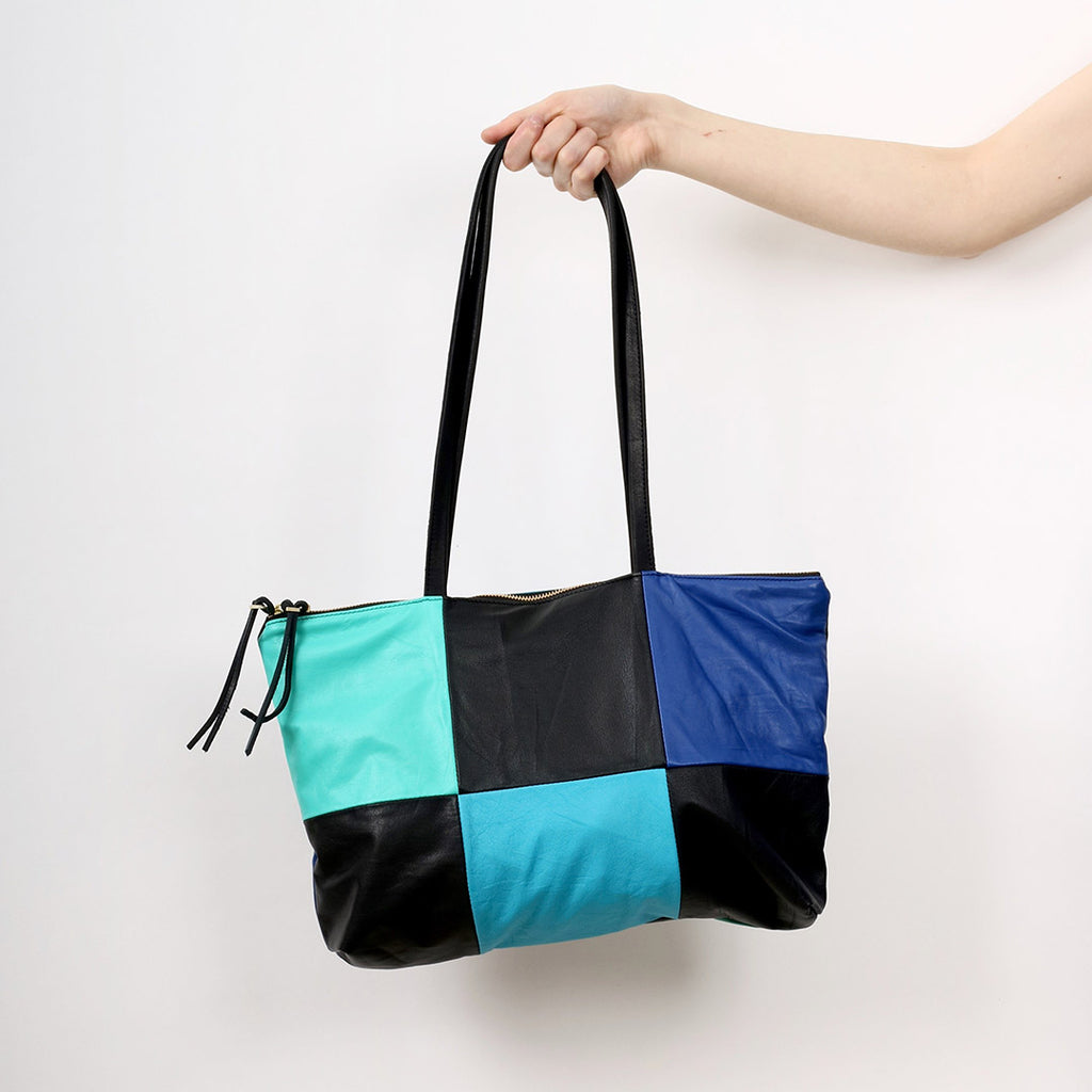 an outreached arm holding a patchwork style leather tote with 6 alternating panels of black and blue leather, a double zip closure and double straps, handmade by erin templeton in vancouver, canada