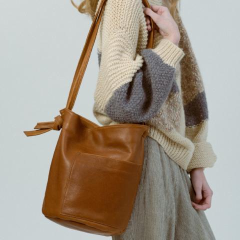 the erin templeton leather bucket bag in caramel, shown on a model wearing a heavy knit sweatshirt