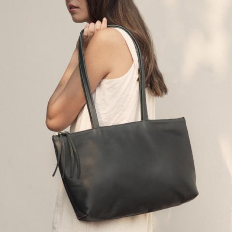 a large 'byob horizon' leather handbag with a zipper closure and secret pocket in black leather, shown on a model wearing cream erin templeton linen overalls on a cream background