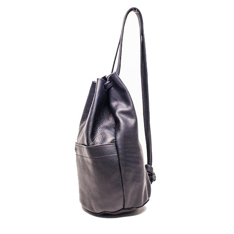 a small gunny sack leather backpack shown from the side in black leather with a gathered strap closure and large front pocket with a stud closure, handmade by erin templeton in vancouver, canada