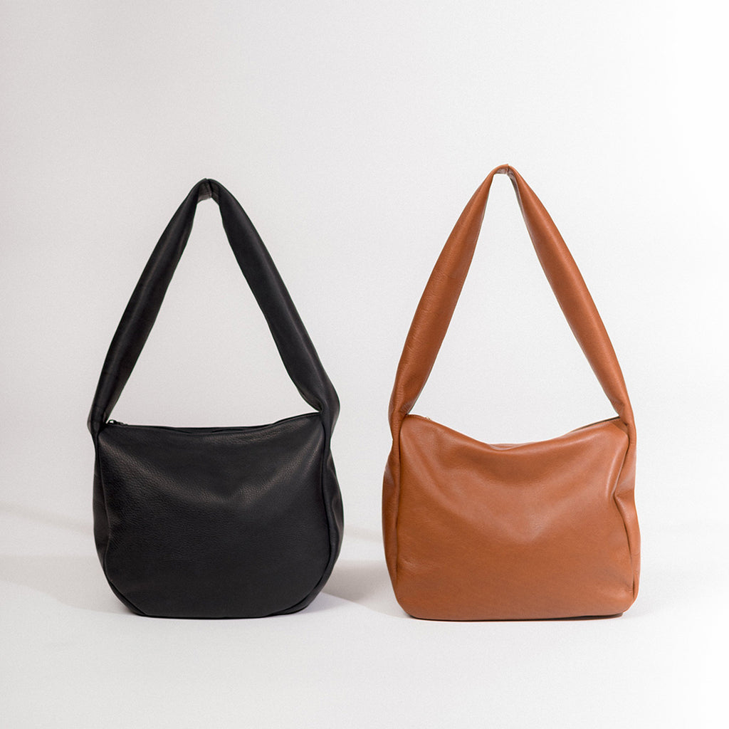 the day tripper leather satchels shown with both a round body in black leather and a square body in caramel leather, both with a zip closure, handmade by erin templeton in vancouver, canada