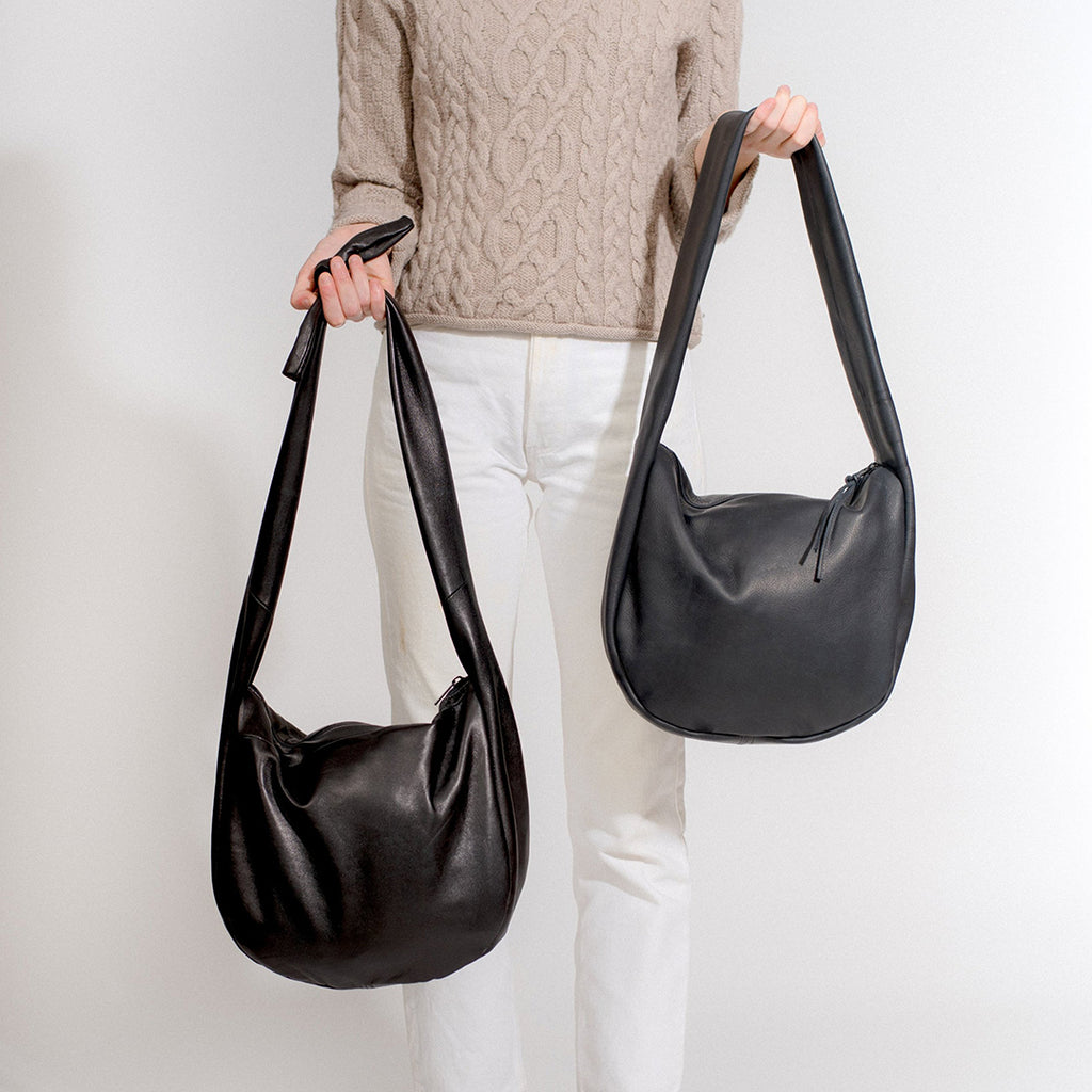 the day tripper leather satchel shown with a round body in both new and recycled black leather with a zip closure, handmade by erin templeton in vancouver, canada