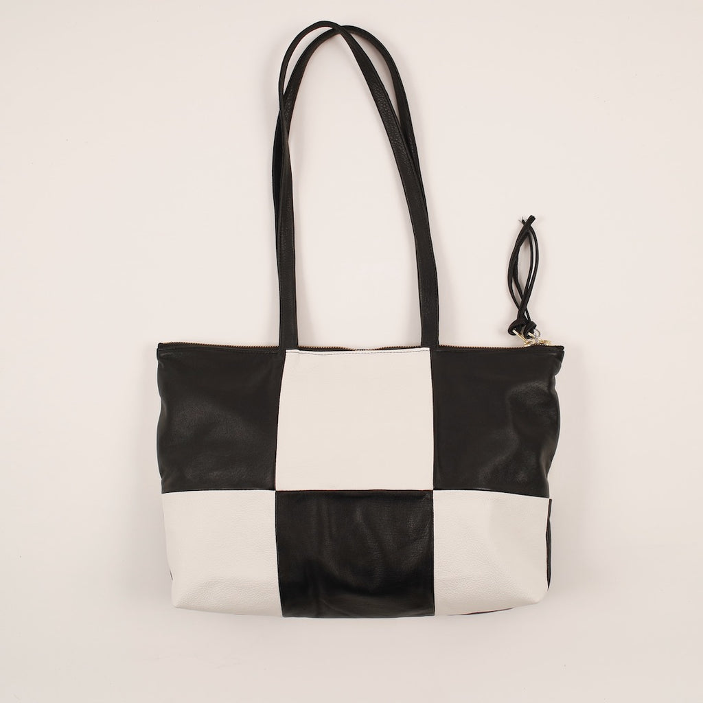 a patchwork style leather tote laying flat with 6 alternating panels of black and white leather, a double zip closure and double straps, handmade by erin templeton in vancouver, canada